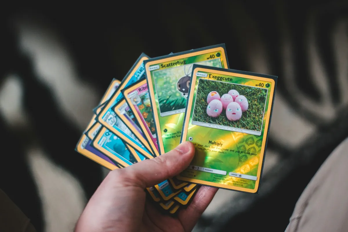 Tay cầm một xấp lá bài Pokémon xòe ra, lá Exeggcute ở trên cùng