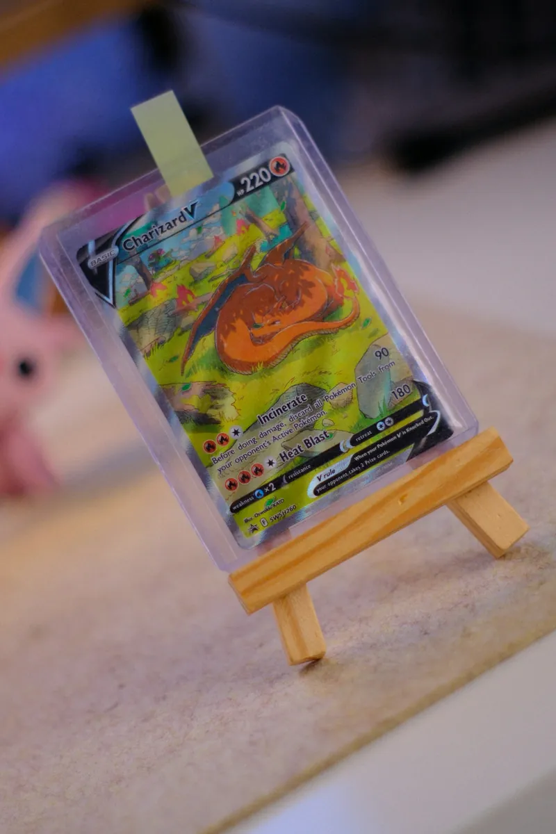Lá Charizard V trong toploader dựng trên giá gỗ nhỏ